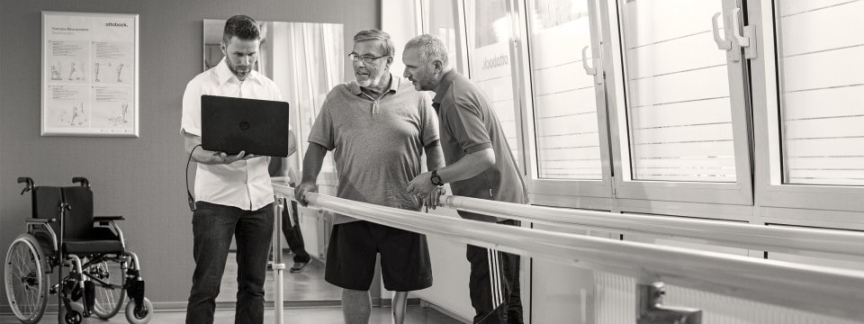 Patient steht mit Therapeut und Techniker in einem Versorgungsraum.