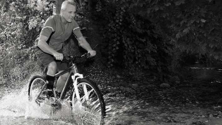 Mann fährt mit seinem Fahrrad durch einen Bach